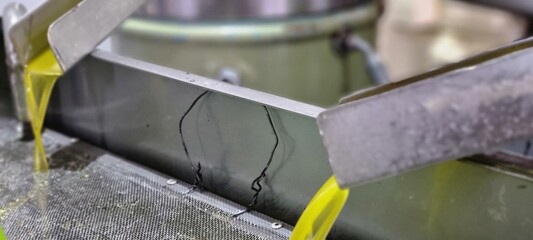 Close-up of fresh extra virgin olive oil flowing from stainless steel pipes during extraction at an olive mill