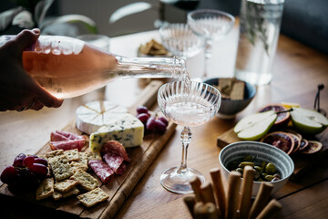 Pouring rose wine with classic snacks of cheese, bread and olives. Party or anniversary celebration.