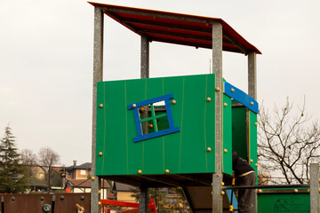Children's play tower with green panels and slide in a neighborhood playground, structural detail and safety railings visible; a community play space portrait in soft daylight.