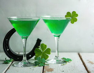 Two green cocktails sit on a rustic table with shamrocks and a horseshoe for Saint Patricks Day. Refreshing drinks prepared for festive holiday.