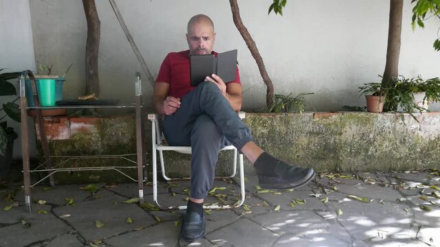 Literature: A man reads an e-reader in the backyard. A person reads an e-book on their e-reader. A man reading a book. Book Day.