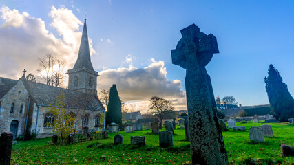 Historic church with ancient cross on green graveyard lawn