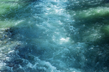 Close-up view of clear river water flowing rapidly with visible ripples and sunlight reflections. Showing the natural motion, freshness and purity of a vibrant mountain stream environment.