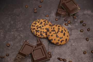 Oatmeal cookies on the table. Pieces of broken dark chocolate. Spilled coffee beans. Dark background. Coffee service. Still life
