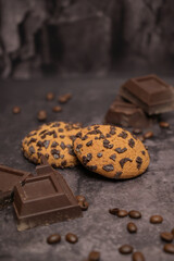 Oatmeal cookies on the table. Pieces of broken dark chocolate. Spilled coffee beans. Dark background. Coffee service. Still life