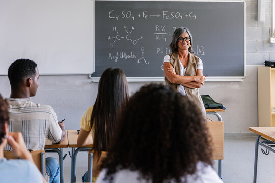 Smiling female teacher standing in front of classroom with students listening. Confident educator leading high school class and sharing knowledge. Education and leadership concept.