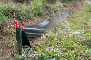 Green erosion control barrier secured with red stakes along a grassy area, designed to prevent soil erosion and manage water runoff in outdoor environments