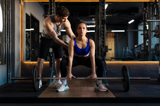 Female athlete practicing lifting weights in gym while man trainer providing guidance, training in well-lit gym, creating motivating environment for fitness