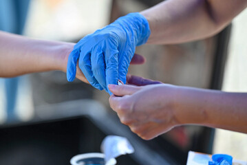 Nurse pricking a patient's finger to perform a blood glucose test