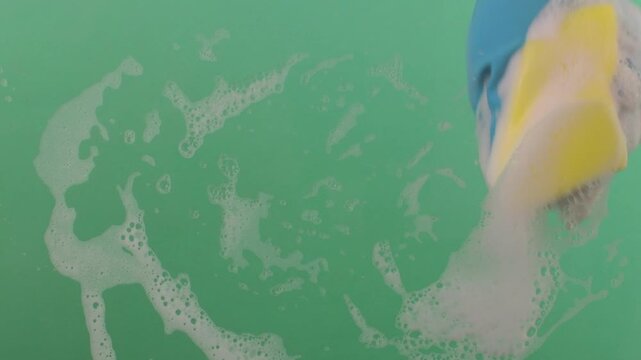 A hand in a rubber glove with a sponge washes the surface. Hands in rubber gloves hold the sponge and scrub the surface. The sponge is covered in sudsy cleanser on a chroma key.