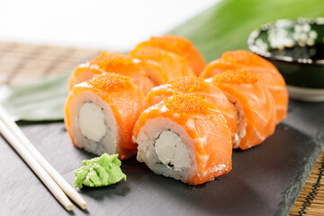 Salmon sushi Philadelphia roll with cream cheese and roe on slate with wasabi and chopsticks