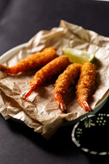 Crispy breaded shrimp with lime on paper in black background, top view