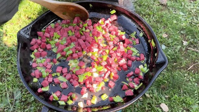 The pleasure of cooking chopped sausage and green peppers in an open-air cast iron pan.