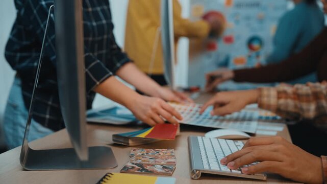 A dynamic office environment showcases teamwork as colleagues discuss strategies around a table filled with charts, computers, and creative materials to enhance collaboration. SACTR