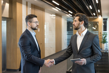Two professional businessmen shaking hands in a modern corporate office, finalizing a partnership deal after a successful meeting, symbolizing agreement and collaboration