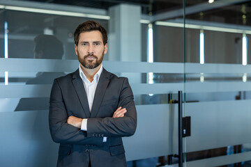 Confident businessman standing with arms crossed in a modern office environment, portraying...