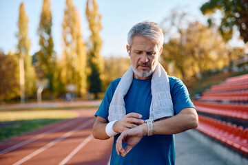Mature runner using fitness tracker at stadium.