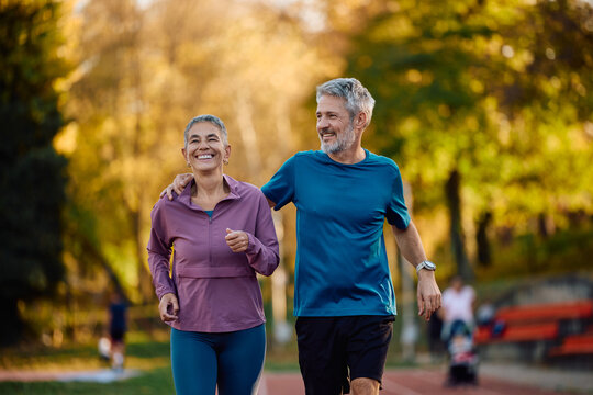 Happy mature sports couple running together in nature in autumn.