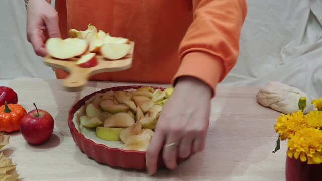 A girl is making apple pie at home. Autumn fall baking background with pumpkins, apples, nuts, food ingredients and seasonal spices. Cooking pumpkin or apple pie for Thanksgiving and autumn holidays, 