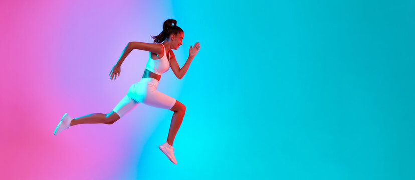 A woman is sprinting energetically, showcasing her athleticism against a bright pink and blue backdrop. She appears focused and determined while wearing a sporty outfit and running shoes.
