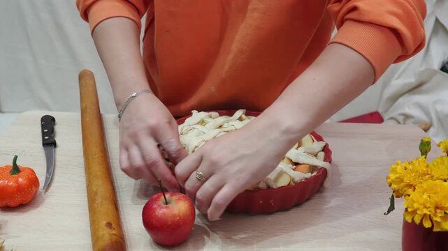 A girl is making apple pie at home. Autumn fall baking background with pumpkins, apples, nuts, food ingredients and seasonal spices. Cooking pumpkin or apple pie for Thanksgiving and autumn holidays, 