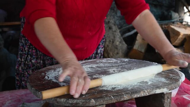 A woman's skill in rolling out dough (thinning dough) using a traditional rolling pin. Quick movements on a floured wooden board.