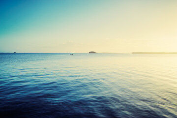 Obraz premium Peaceful Ocean Scene with Gentle Waves and a Distant Island at Sunrise