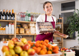 Young female seller at counter offering sweets in grocery store