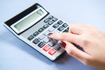 Woman's hand using calculator on blue background.