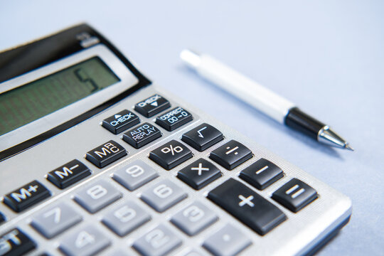 Gray calculator and white pen on blue background.