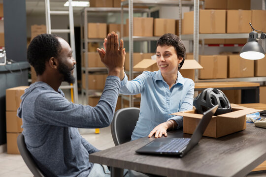Multiethnic workers team sharing a high five after achieving delivery goals, reflecting teamwork and success in a logistics center depot and storage room. Joyful warehouse moment.