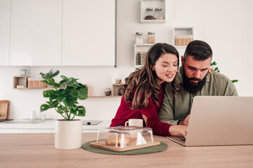 Couple planning online trip using laptop in kitchen