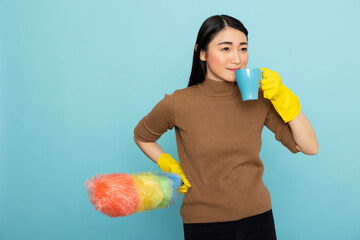 Smiling housekeeper holding colorful brush and drinking coffee against isolated background. Asian...