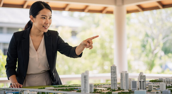 asian businesswoman presenting architectural model of modern city in office setting - Powered by Adobe