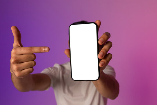 A young man holds a smartphone near his face, pointing at the empty screen. The setting features neon lights, showcasing space for a mobile app or website design. - Powered by Adobe