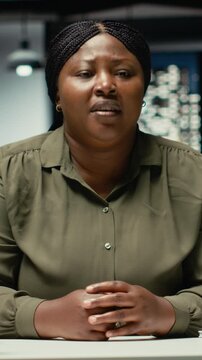 Vertical Video General manager waving at laptop during a teleconference with investors, engaged in a digital discussion. Female worker staying after hours, interacting via video call connection