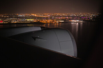 View of the aircraft engine nacelle from the airplane window with a city at night in the background.