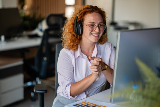 Smiling businesswoman with headphones working at modern office desk