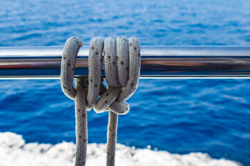 Close up of a rope tied in knot around metal rail, sea background