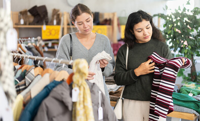 In store, Latin woman and female friend customer chooses autumn sweater. Creating capsule wardrobe, branded clothing at affordable prices. Modern urban fashion, casual practical clothes