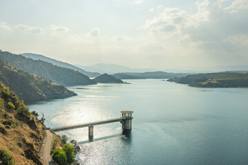  Panoramic view of a reservoir surrounded by green forests with the sun filtering through the clouds above the water