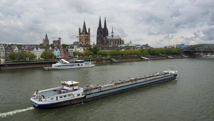 View of transport ship on the Rhine River heading North going past Old Town K&ouml;ln (Cologne) waterfront, St. Martin Church, and,The K&ouml;lner Dom as seen from the Deutzer Br&uuml;ke.