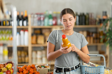 Young woman buyer chooses fresh peach juice in bottle in grocery store