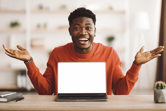 A young man in a red sweater is smiling broadly while gesturing with his hands in front of a laptop. He is in a bright, comfortable indoor setting, suggesting a cheerful mood. - Powered by Adobe