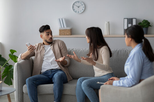 In a therapy room, an Arab woman discusses her husband's smartphone addiction with a psychotherapist. The couple seeks help for their relationship issues related to technology overuse.