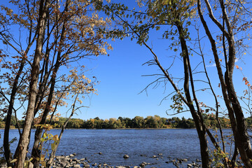 A calm river framed by early autumn foliage and blue sky in Laval, Quebec. The scenic composition highlights the balance between nature and suburban landscape in fall.