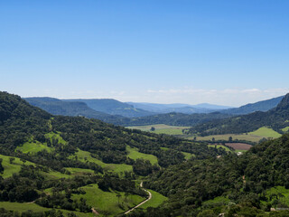Fototapeta premium Panoramic view of green mountain valley with forested hills and clear blue sky in the countryside of southern Brazil, ideal for nature and travel themes