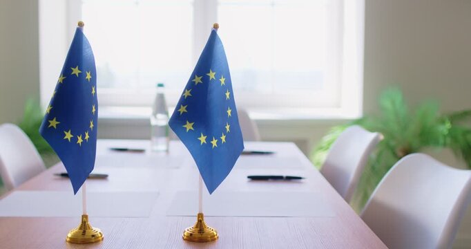 EU flag signals negotiations, euro policy and law. Desk flags on a bright conference table imply parliament talks and diplomacy and decision-making. Symbol of European legislative meeting.