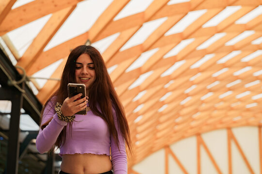 Young woman smiling using smartphone under wooden structure