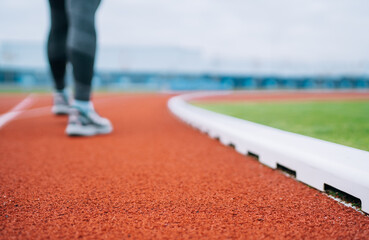 Modern athletic stadium with red rubber running track close-up and blurred sporty female legs in running shoes ready for long walk or jog, healthy lifestyle, active women fitness and outdoor activity